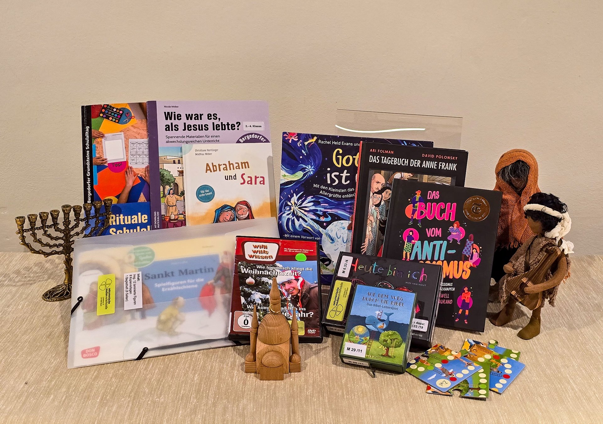 Foto von verschiedenen Medien und Gegenständen, die bei uns ausleihbar sind, wie zum Beispie: Bücher, Schwarzenberger Figuren, Spiele, Erzählschienen-Figuren, DVD, Bildkarten, Chanukkia